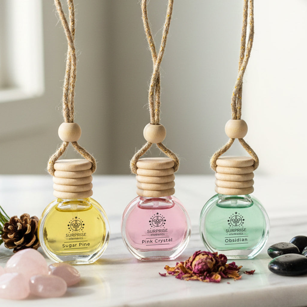 Three small car fragrances bottles with wooden tops on a white surface with decorative elements and surprise elements logo.