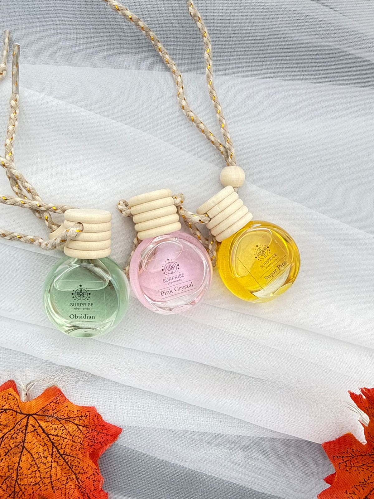Three small bottles of perfume on a white fabric background with autumn leaves.