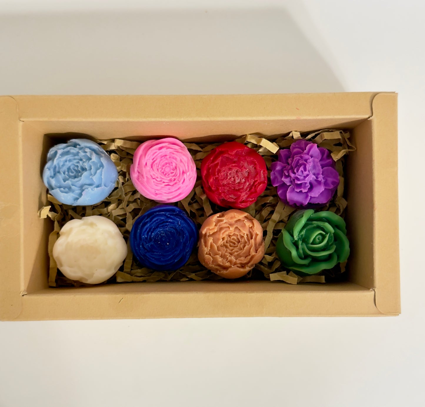 Set of colorful flower-shaped wax melts in a cardboard box on a white background