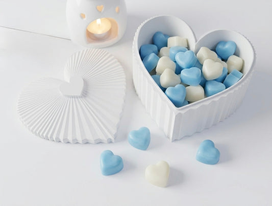 Heart-shaped container filled with blue and white heart-shaped wax melts on a light surface.