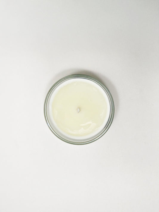 Small glass jar with a white candle on a light gray background