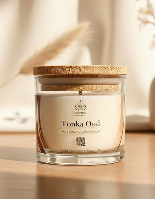 Candle labeled 'Tonka Oud' surprise elements logo clear jar with a bamboo lid on a neutral background text written on the label is 4oz coconut wax candle hand-poured in Houston Texas 