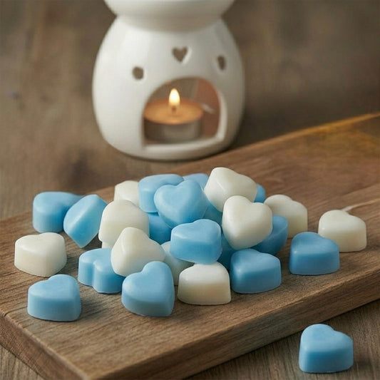 Heart-shaped blue and white wax melts on a wooden surface with a white ceramic warmer in the background.