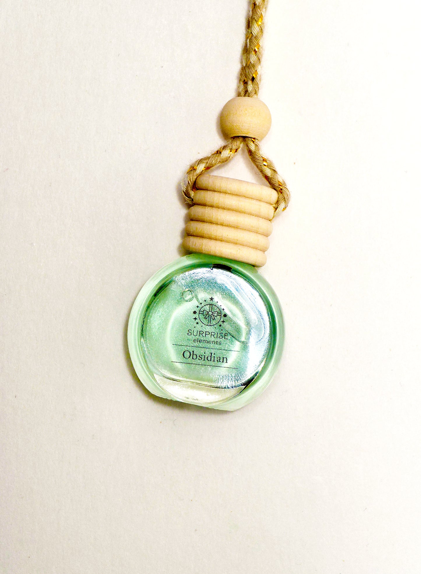 car fragrance clear bottle-shaped pendant with wooden top on green liquid in it and surprise elements logo on the bottle and a beige background 