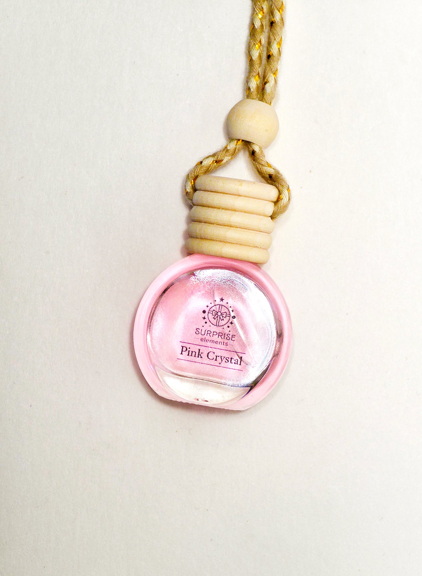 Pink crystal car fragrance bottle charm with wooden accents on a light background