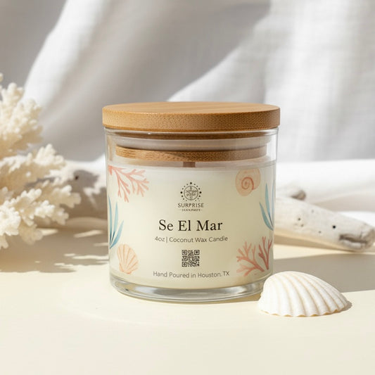Candle jar labeled 'Se El Mar' with a bamboo lid on a sandy background 4oz coconut wax candle hand-poured in Houston Texas label with surprise elements written on it with the logo 