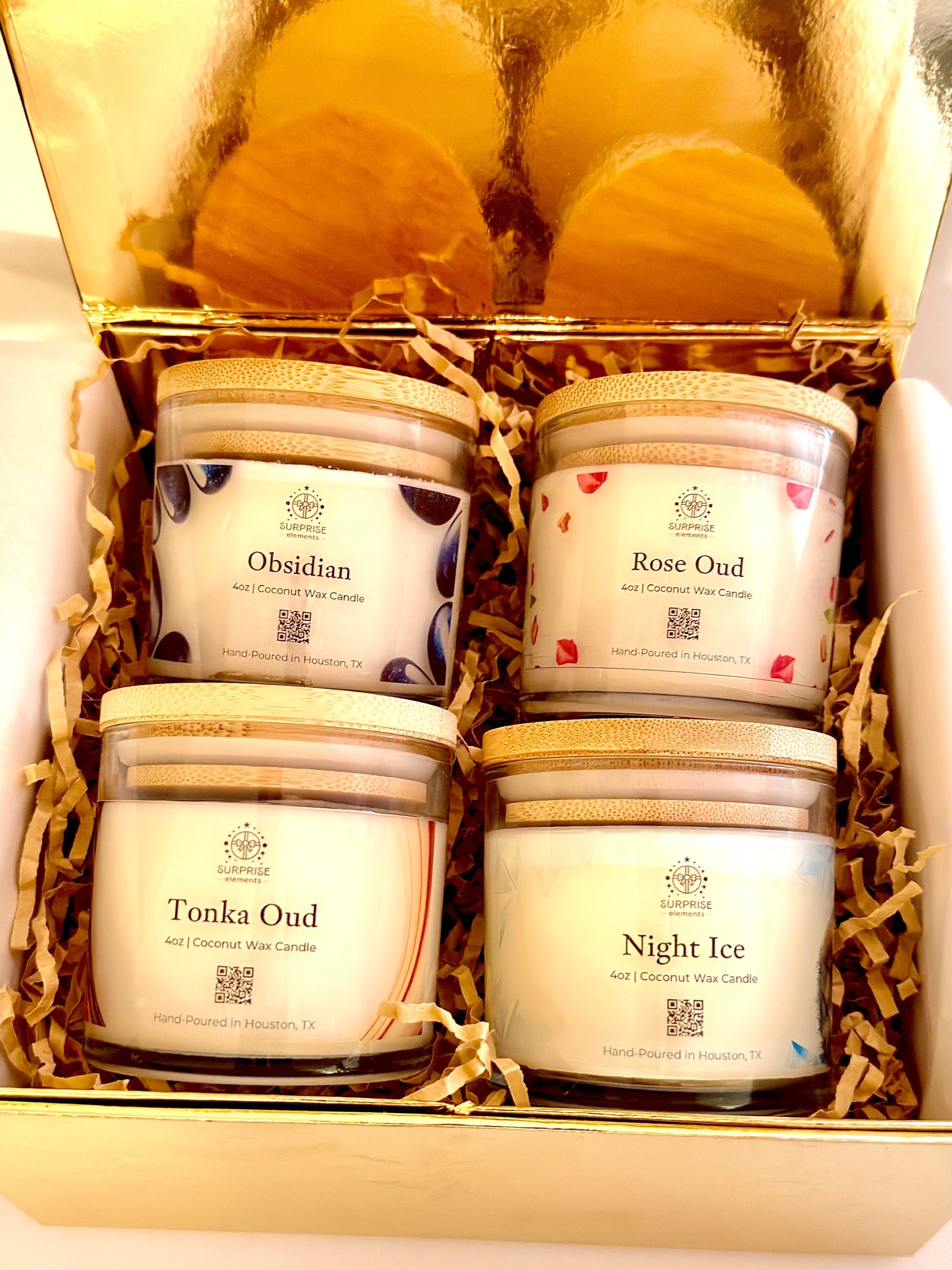 Four scented candles in a decorative box with visible labels. 